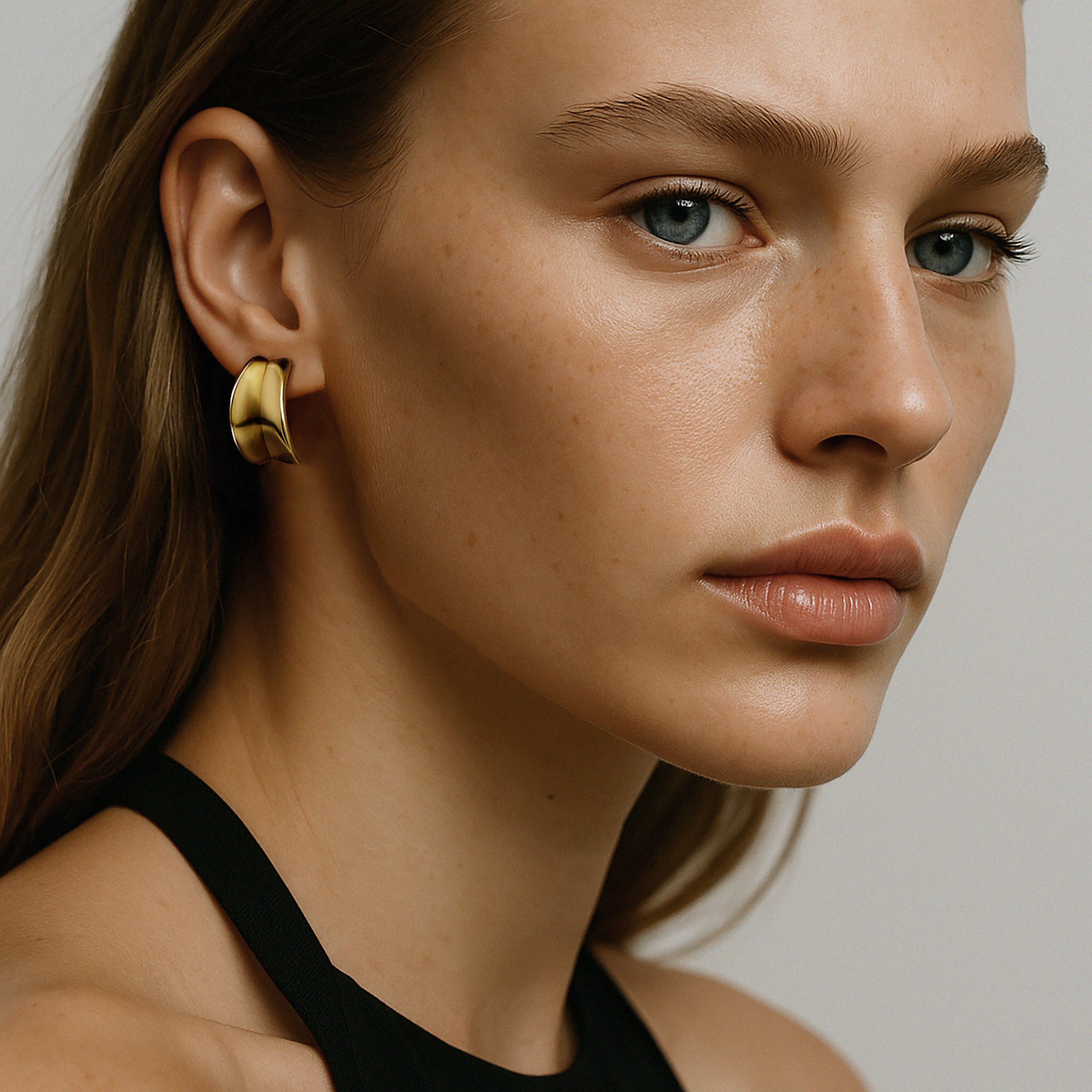 Bizou SF253E001GL – Woman wearing gold chunky curved stainless steel hoop earrings, side profile, Bizou jewelry
