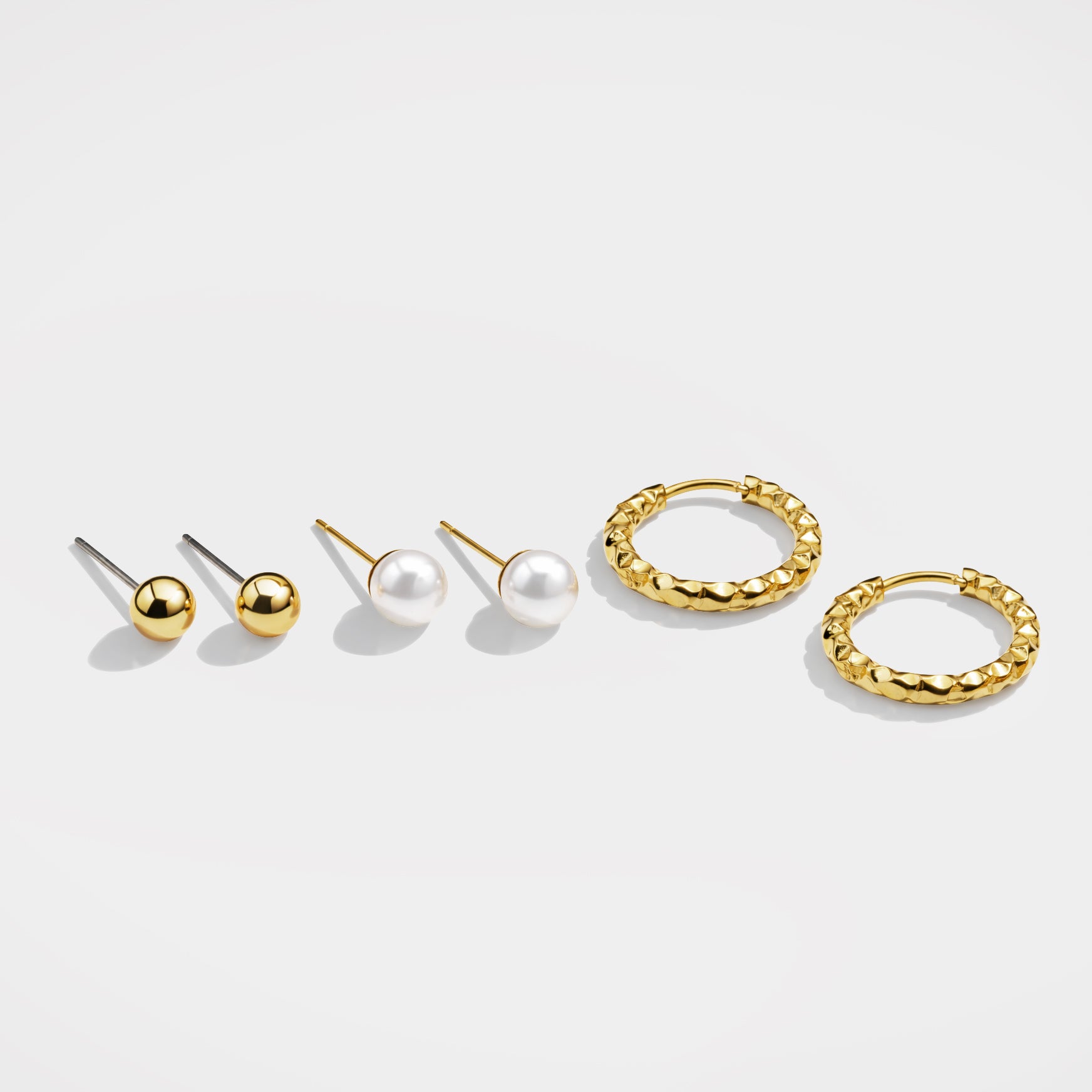 Bizou SF253E006GL – Gold 3-piece earring set with ball studs, pearl studs and textured hoop earrings in stainless steel, angled view, Bizou jewelry