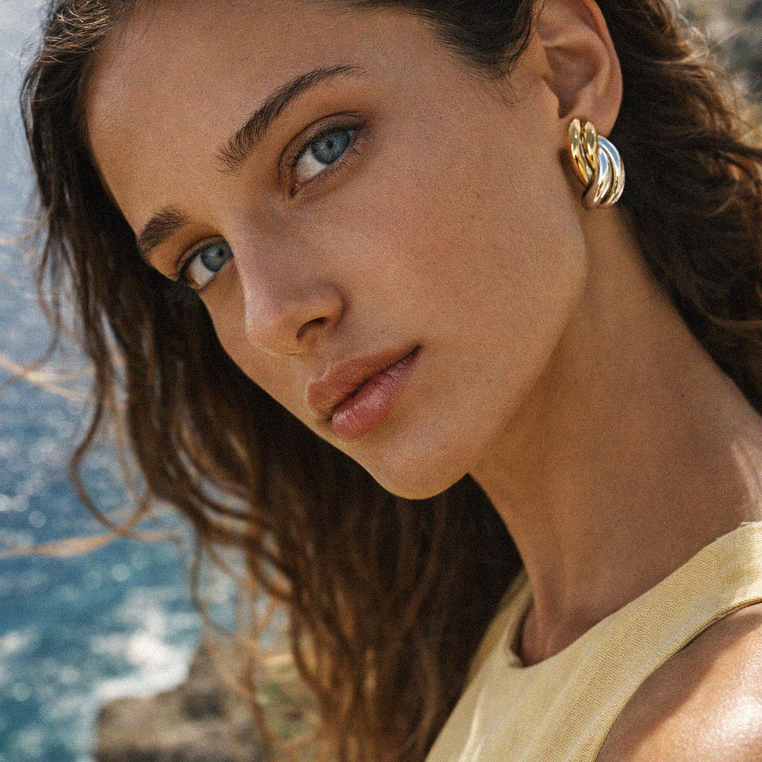 Bizou SF253E014MM – Woman wearing two-tone gold silver stainless steel knot earrings by the sea, Mediterranean lifestyle, Bizou jewelry