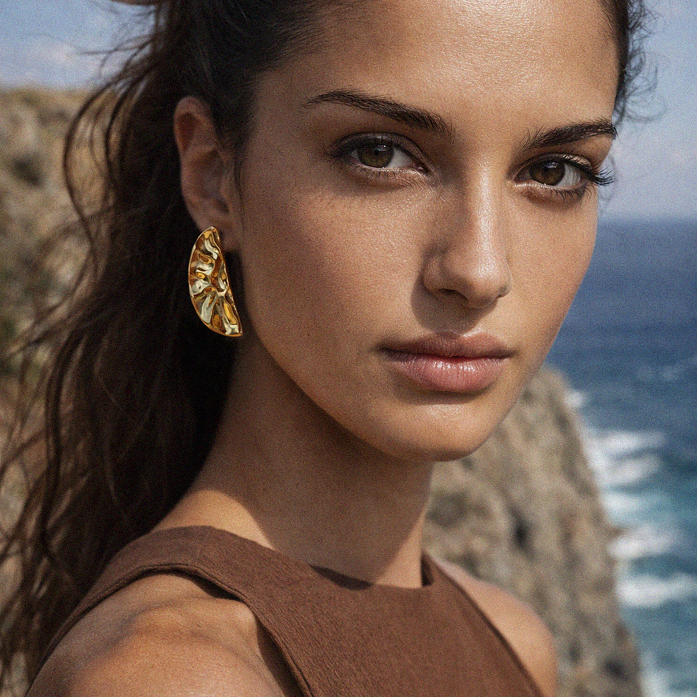 Bizou SF253E009GL – Woman wearing gold hammered half-moon statement earrings by the sea, Mediterranean lifestyle, Bizou jewelry