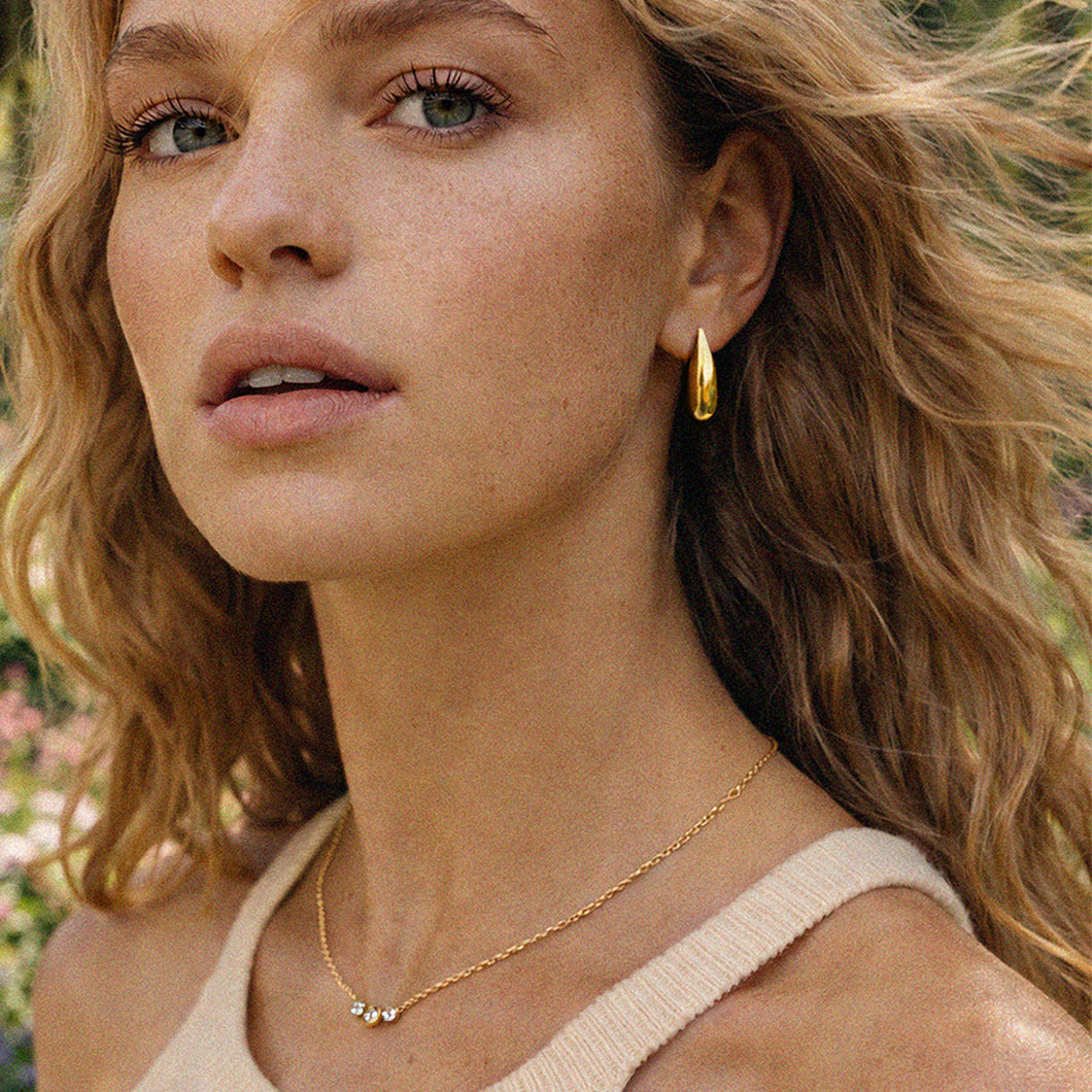 Bizou SS253N014GL – Woman wearing gold stainless steel triple CZ bezel necklace on delicate chain, styled with gold hoop earrings, Bizou jewelry

