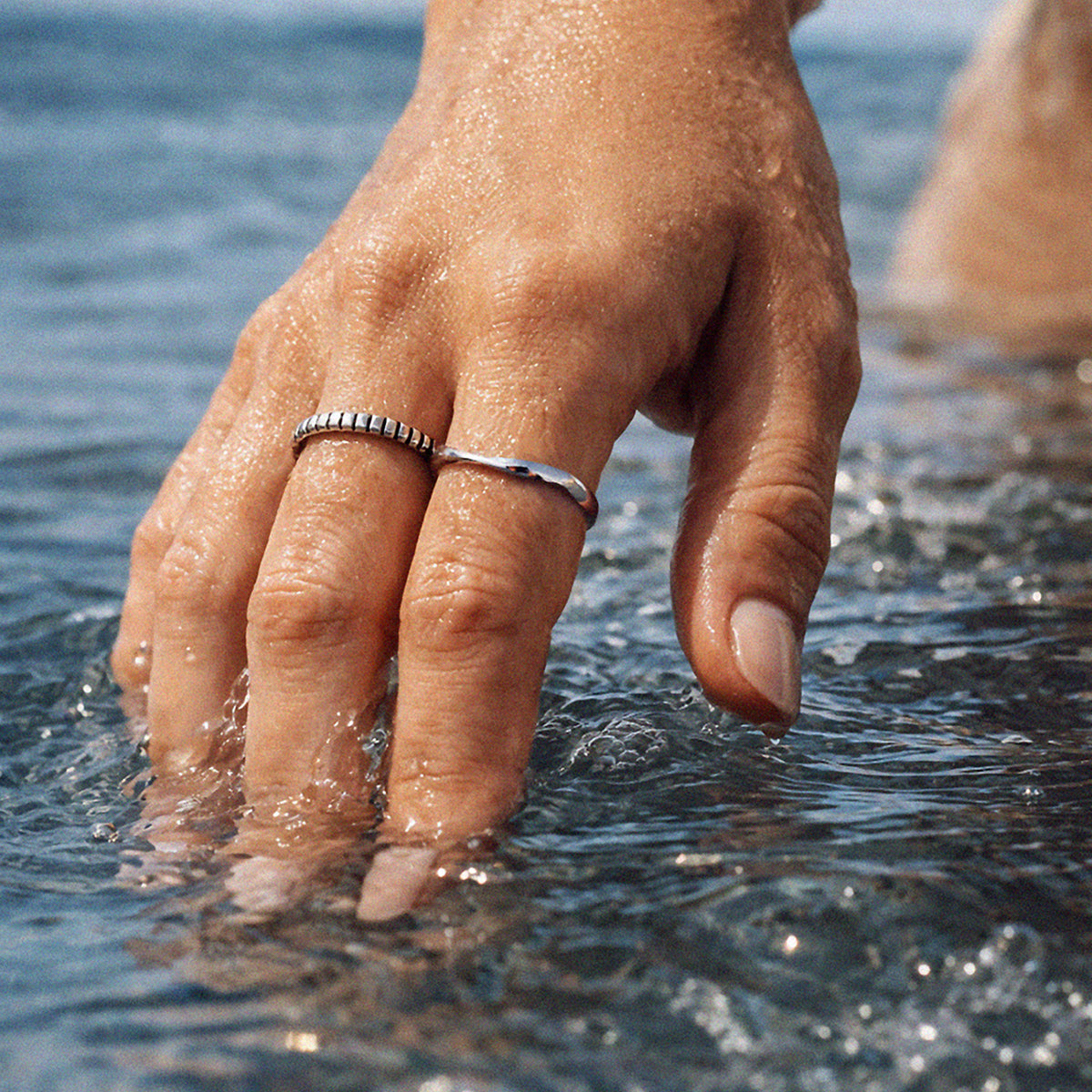 Bizou SS253R022SL – Woman wearing silver stainless steel vertical groove band ring in water, stacked with second ring, side view, Bizou jewelry

