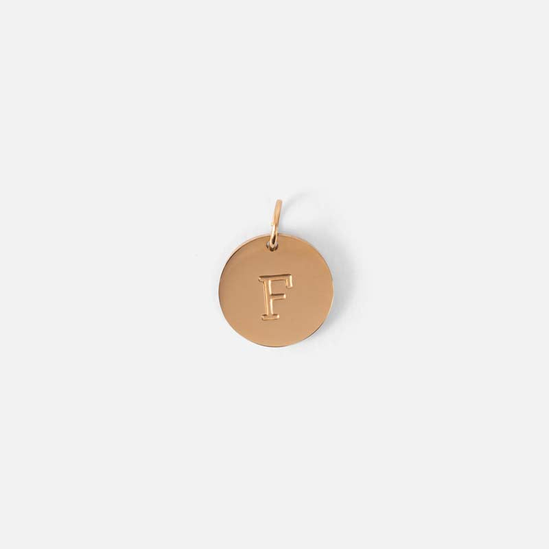Small symbolic golden charm engraved with the letter of the alphabet "f"