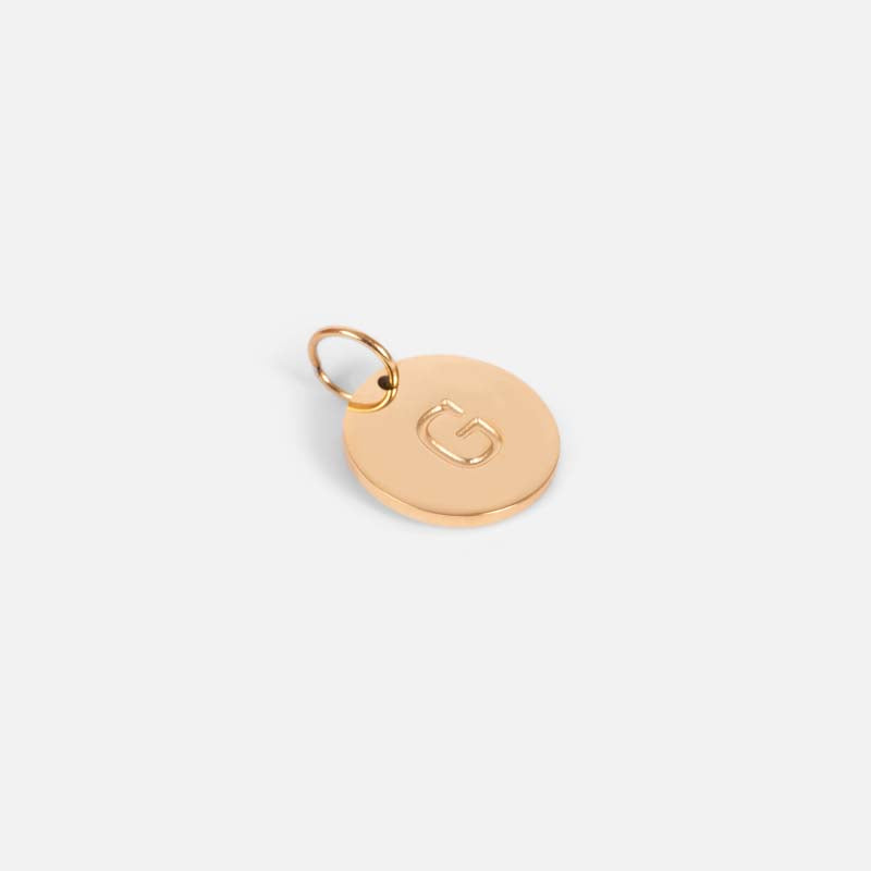 Small symbolic golden charm engraved with the letter of the alphabet "g"