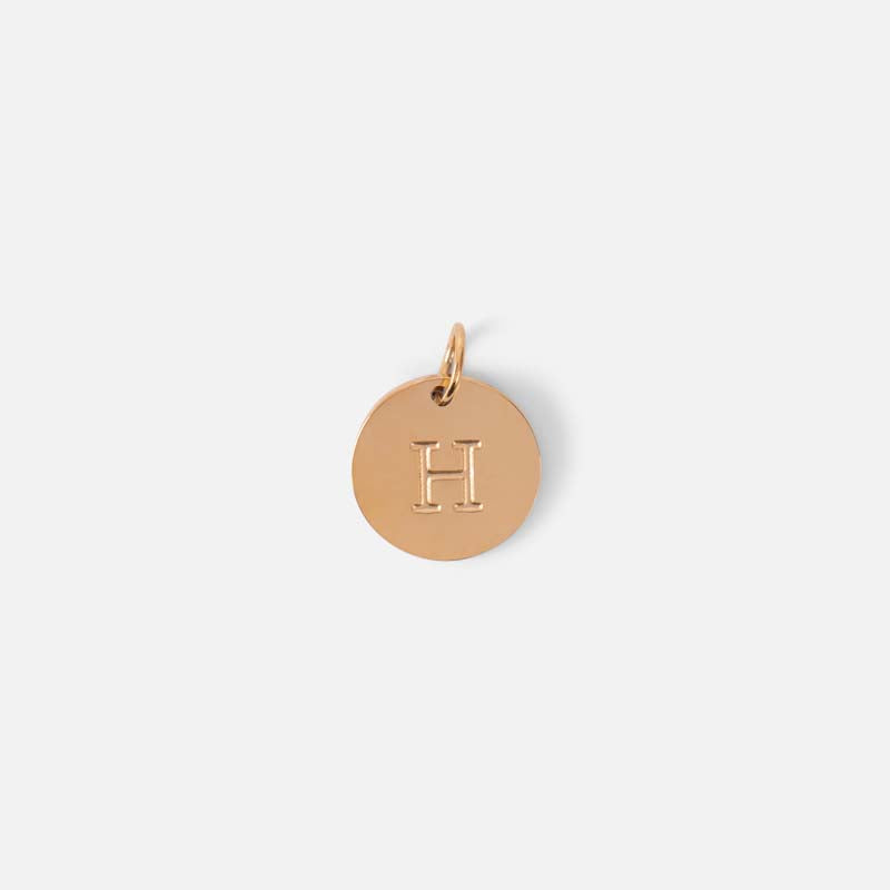 Small symbolic golden charm engraved with the letter of the alphabet "h"