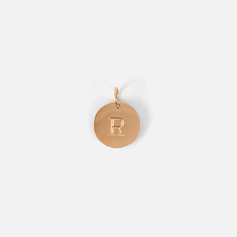 Small symbolic golden charm engraved with the letter of the alphabet "r"